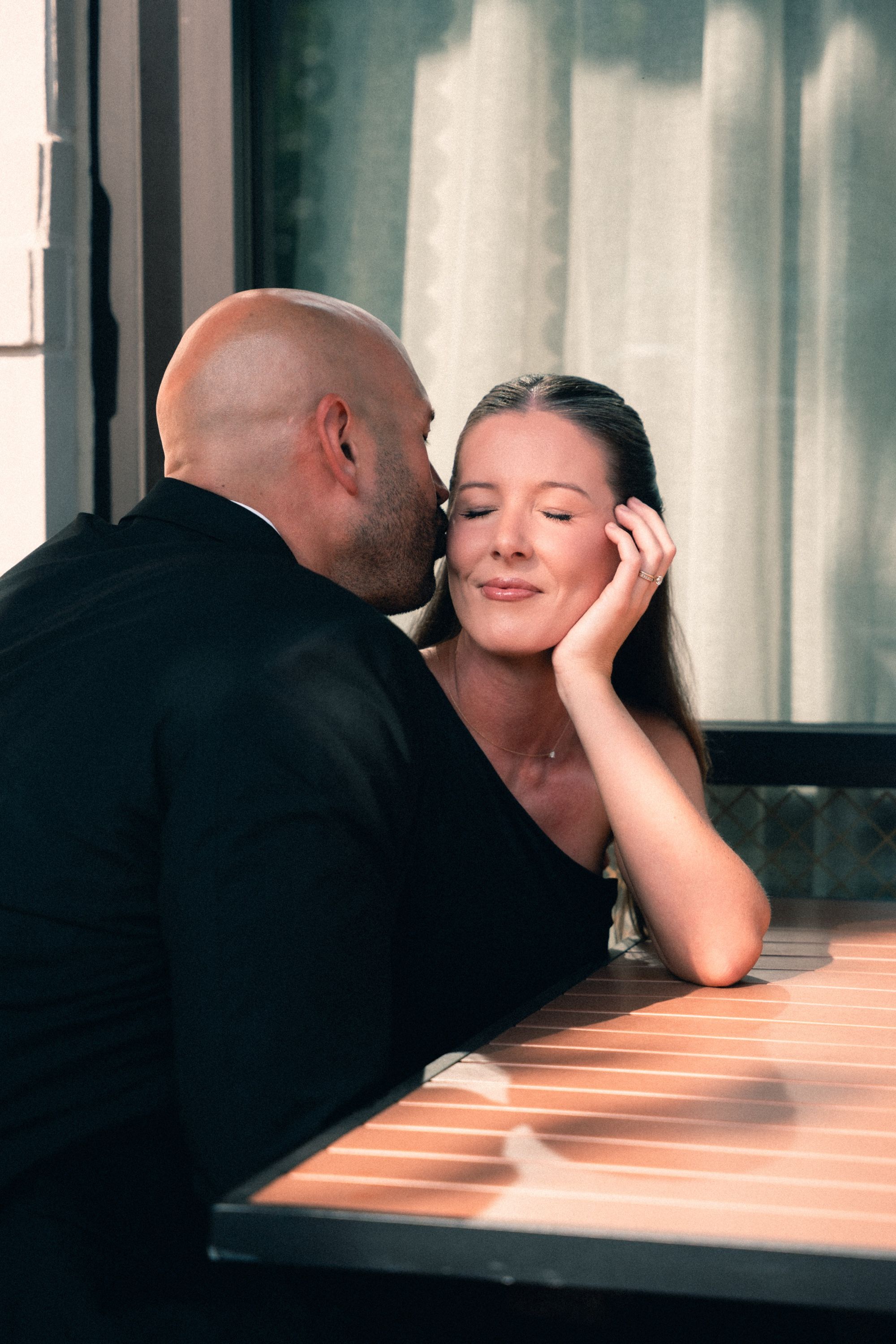 Couple sharing a kiss at a terrace table in evening light, Memphis engagement photography by Atkinson Studio