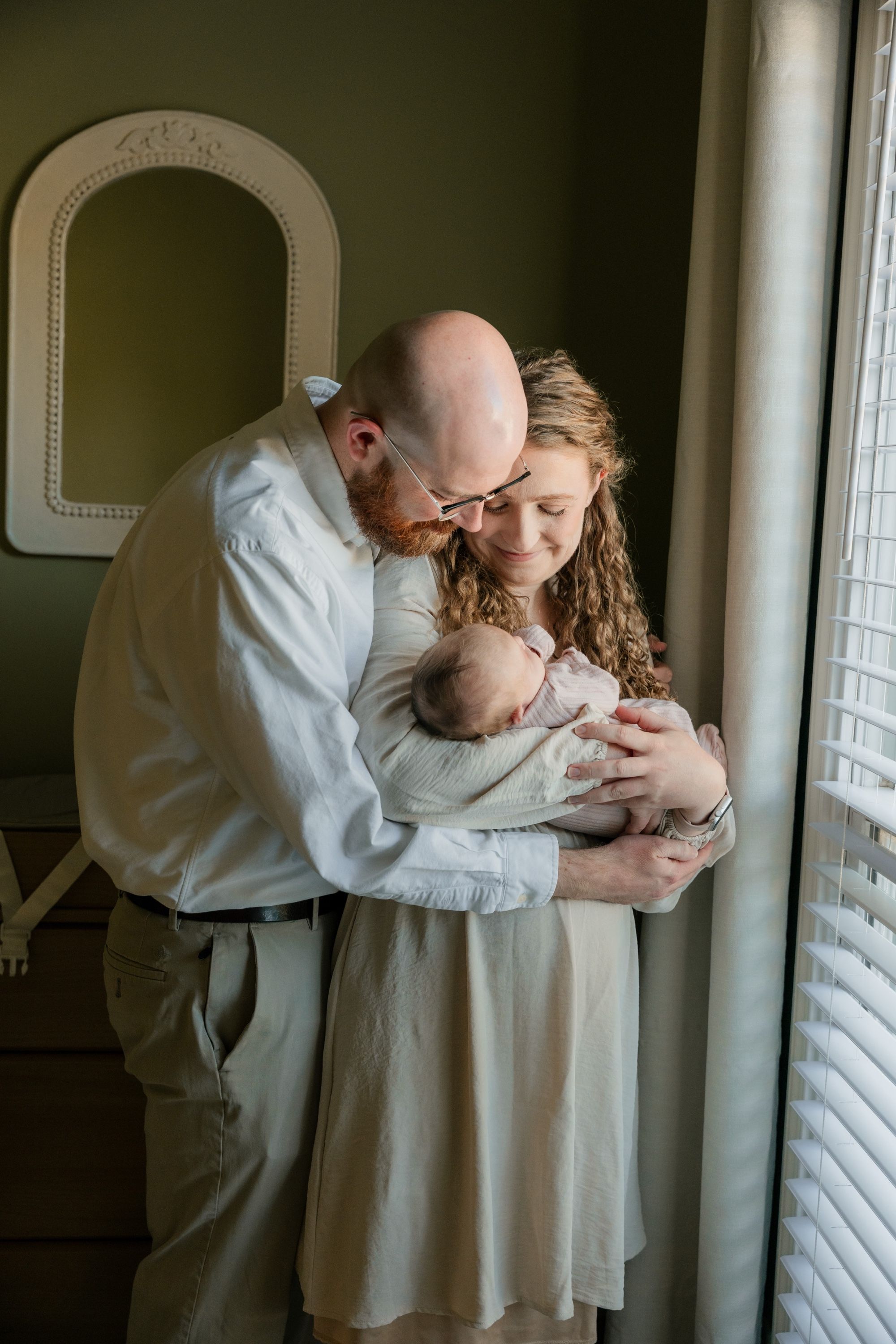 Newborn photo of parents holding their baby by a window, Memphis family photography by Atkinson Studio