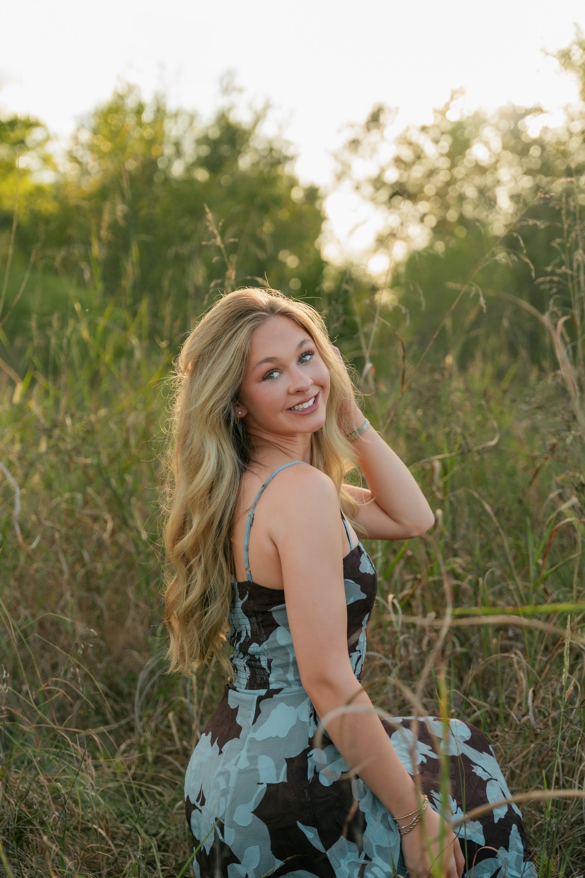 Senior smiling over her shoulder in tall grass, Memphis senior portraits by Atkinson Studio